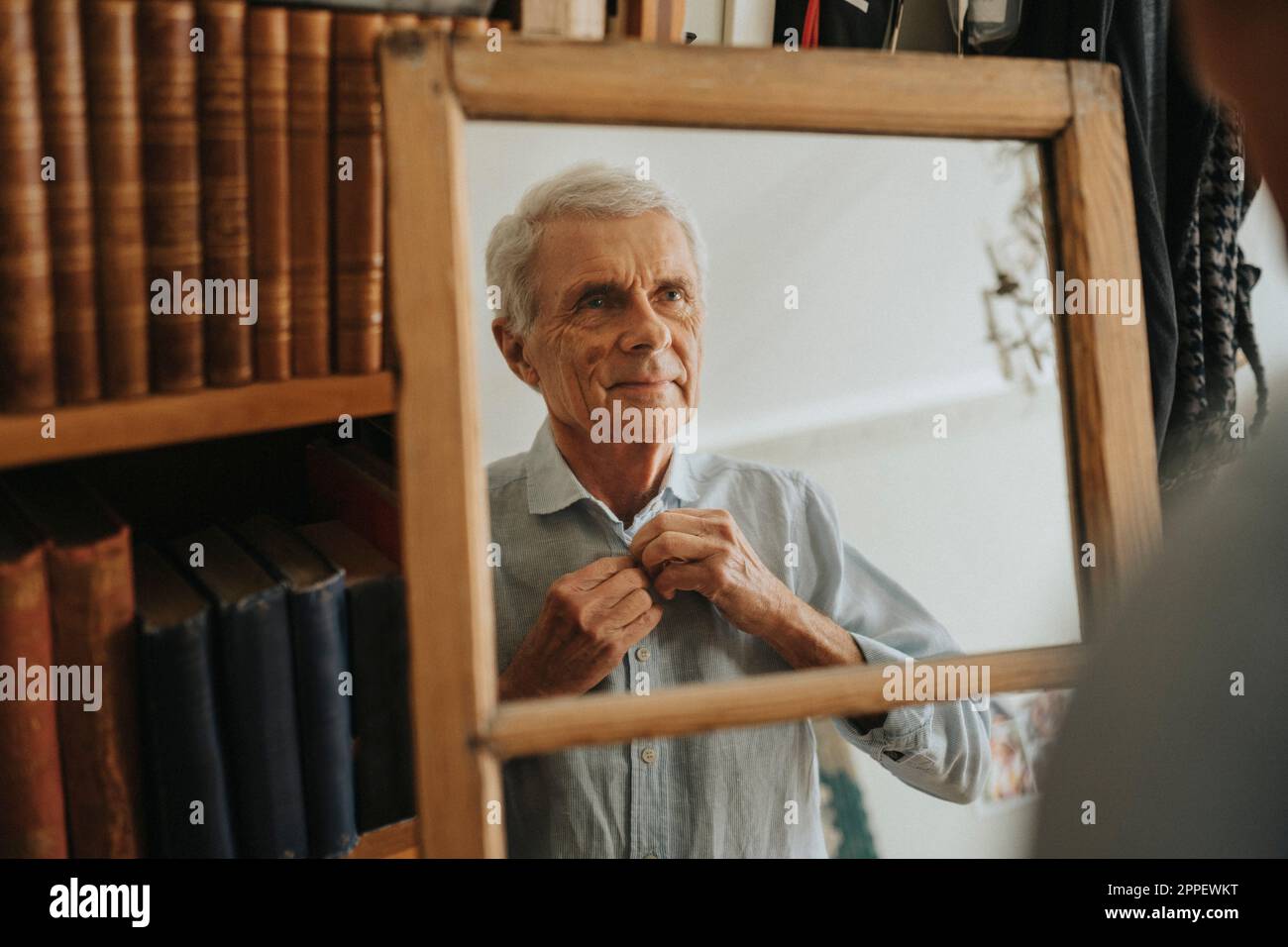 Senior man looking in mirror and buttoning shirt Stock Photo