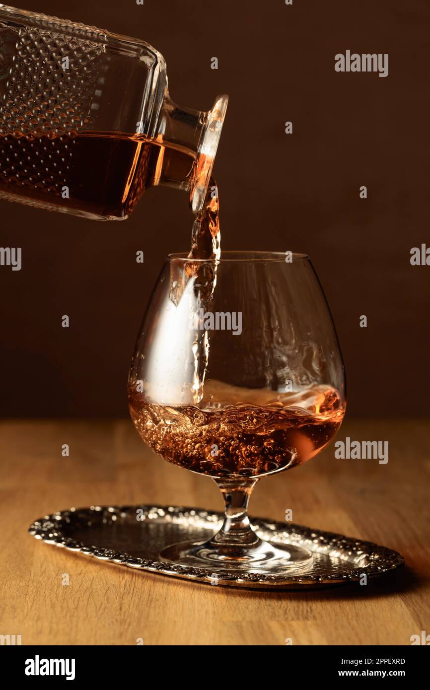 Brandy is poured from a decanter into a snifter glass. Cognac on an oak