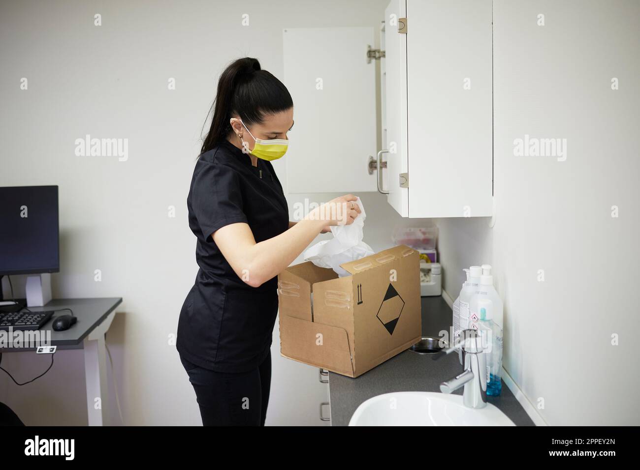Female dentist in surgery putting supplies in cupboard Stock Photo