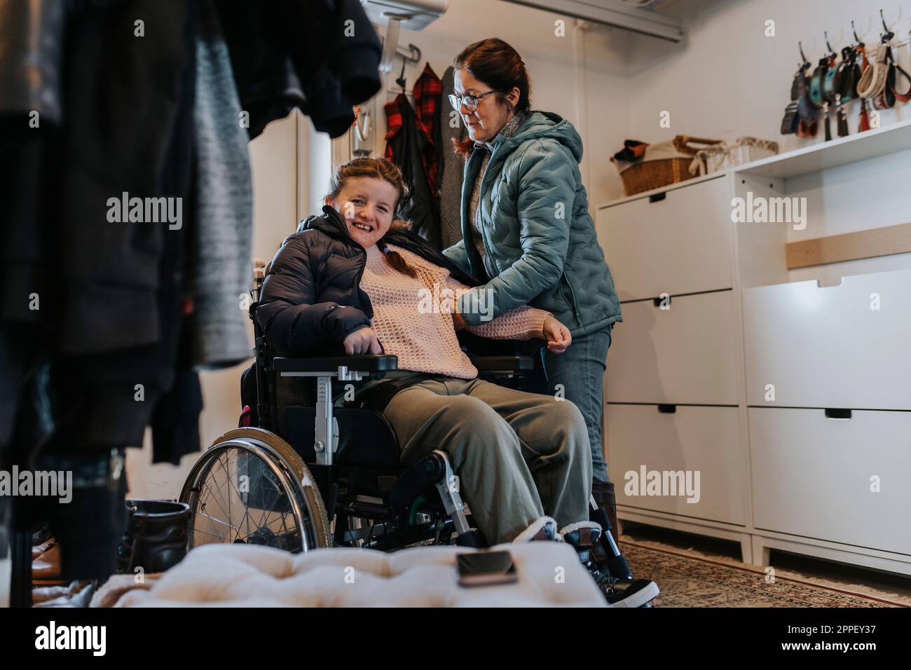 Mother helping daughter on wheelchair taking coat off Stock Photo Alamy