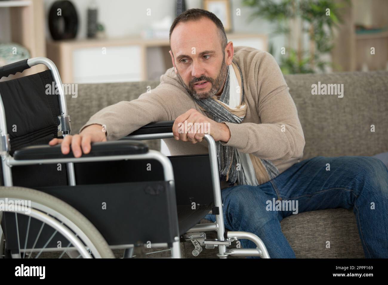 man trying to reach his wheelchair Stock Photo