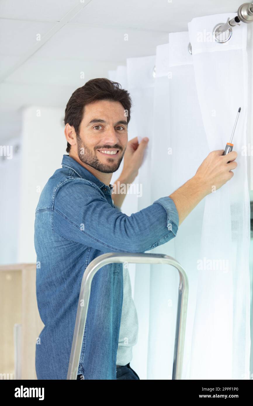young man installing curtains over window Stock Photo