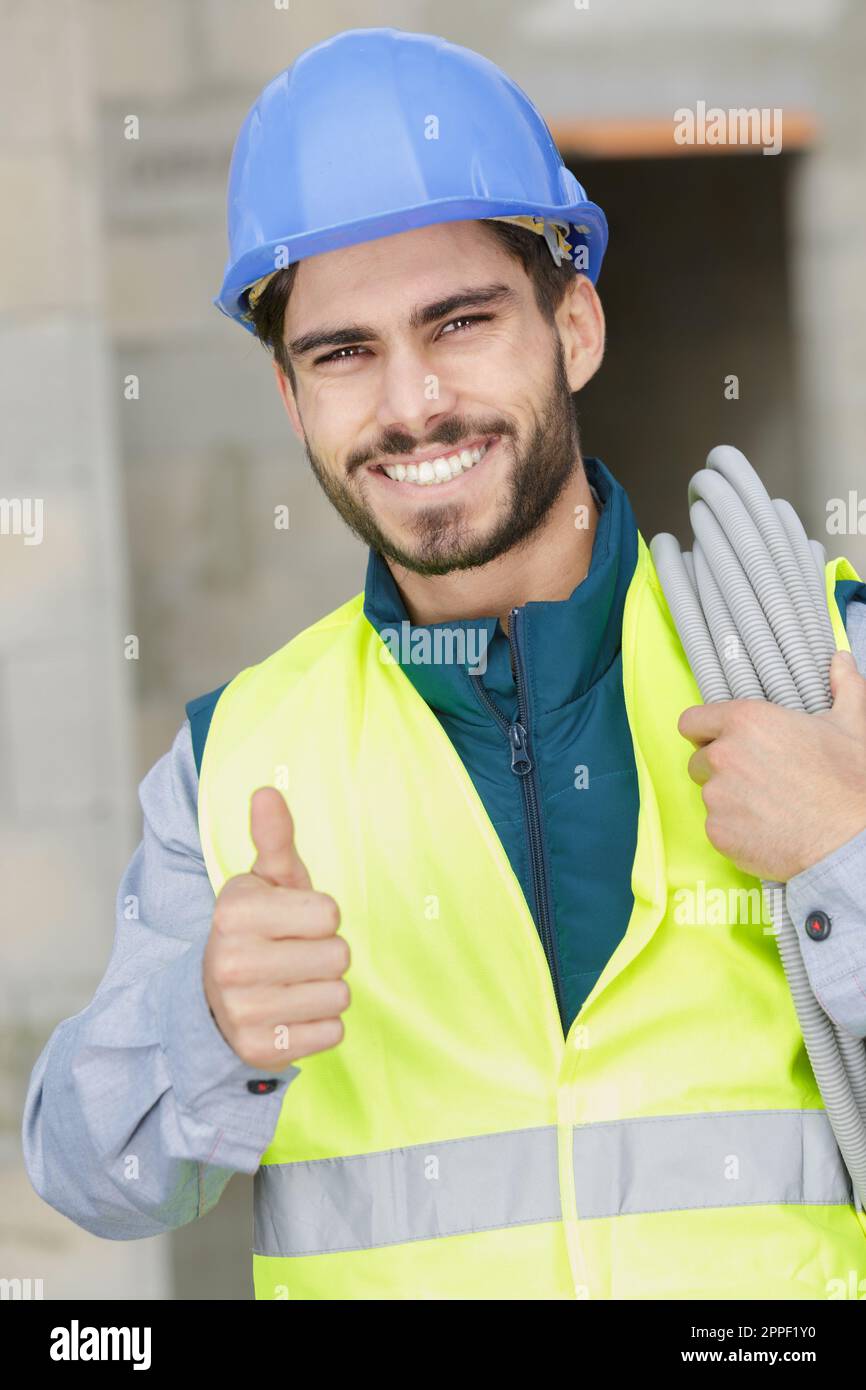 cheerful constructor with electric cable showing thumb up Stock Photo