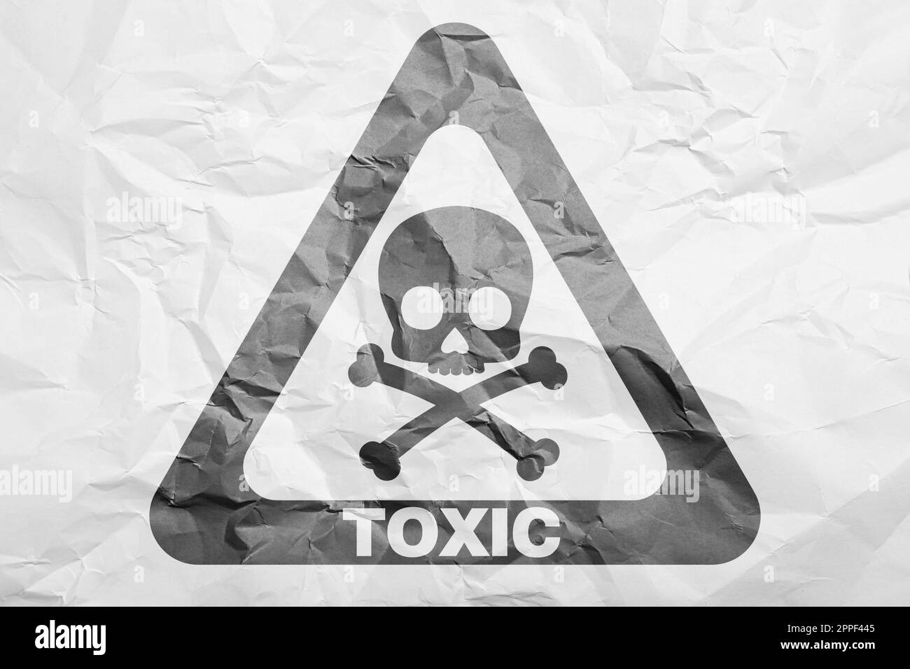 Hazard warning sign (skullandcrossbones symbol and word TOXIC) on crumpled white paper, top