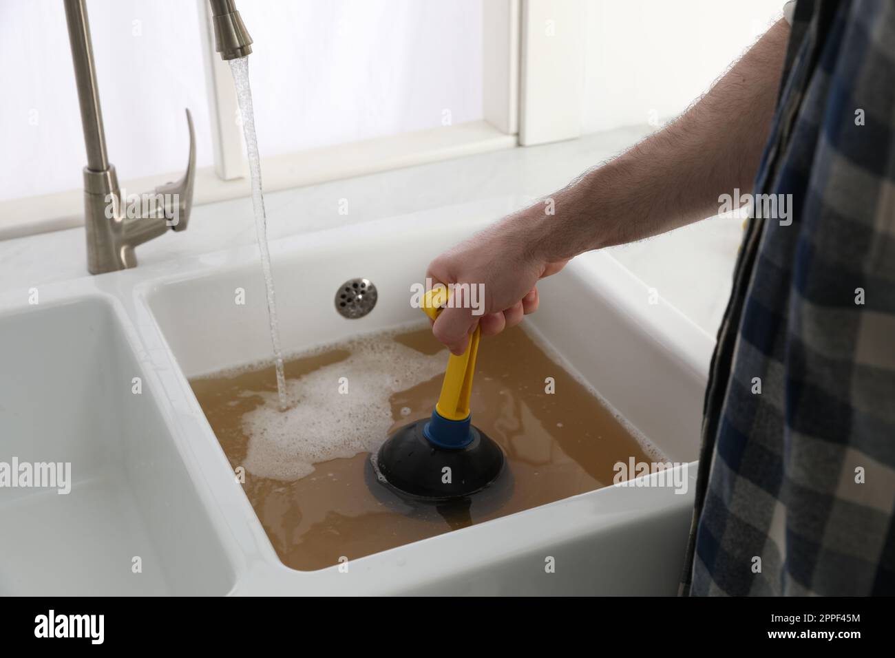 Man using plunger to unclog sink drain in kitchen, closeup Stock Photo