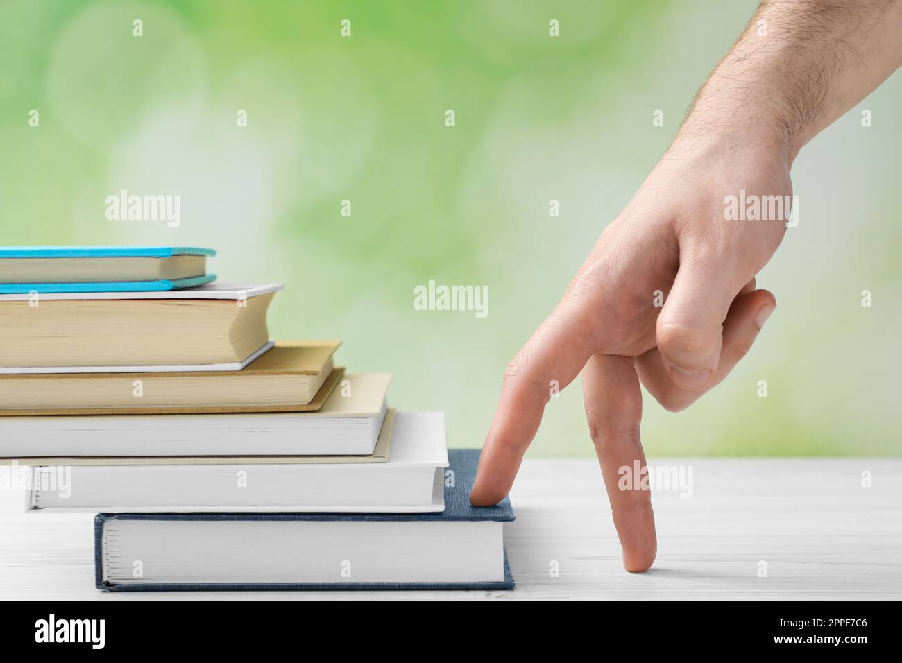 Man climbing up stairs of books with fingers on white wooden table against blurred background, closeup Stock Photo