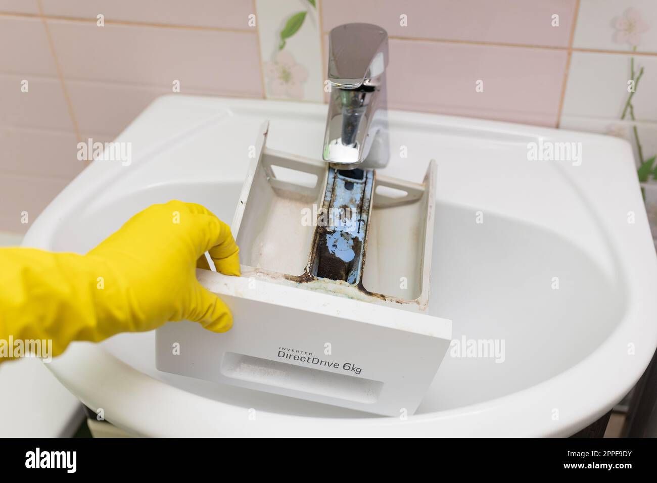 Hand in yellow glove washing, cleaning dirty laundry machine dispenser