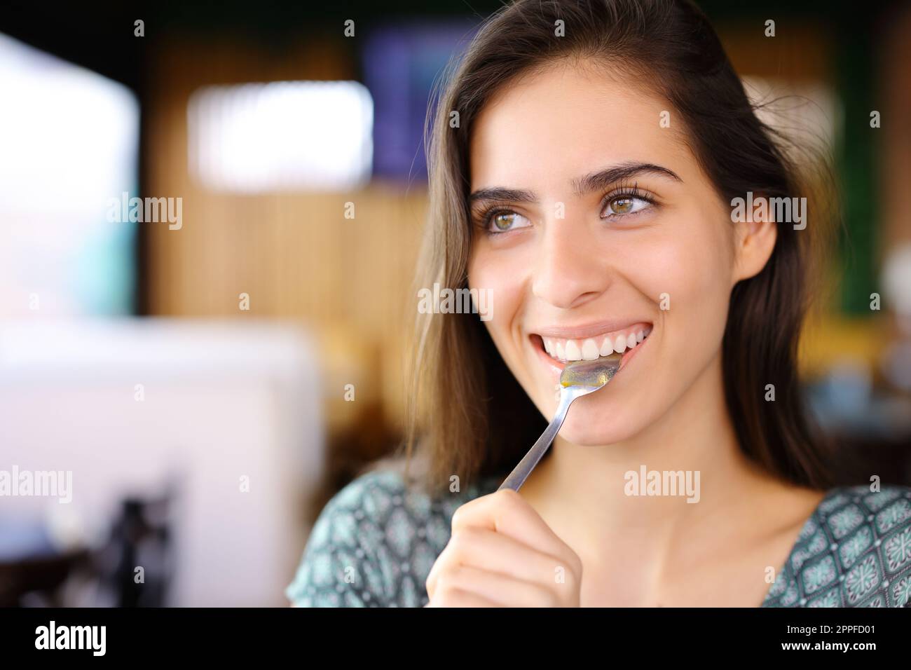 Happy woman with spoon in mouth looks away in a restaurant Stock Photo