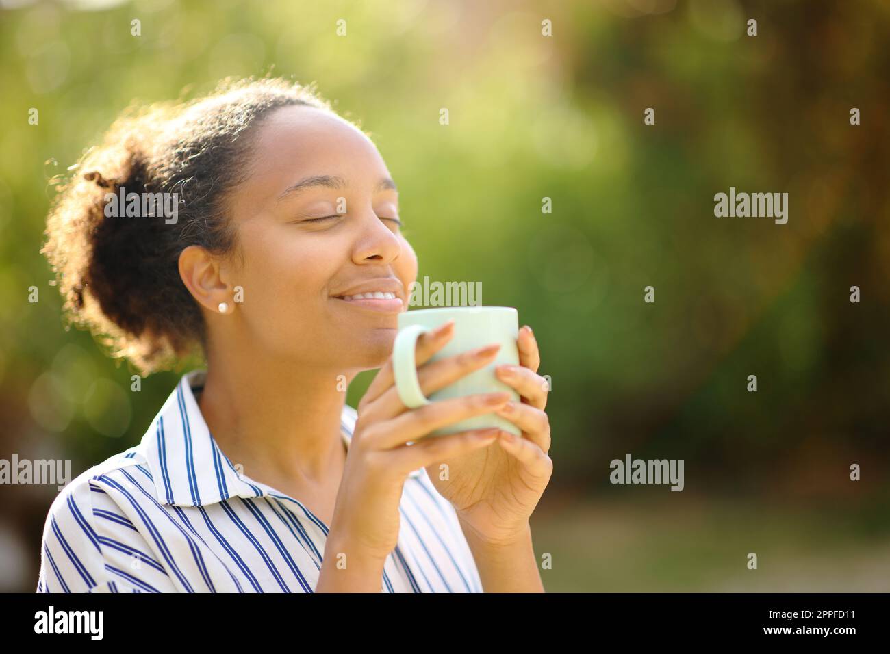 Relaxed black woman smelling coffee cup resting in a park Stock Photo ...