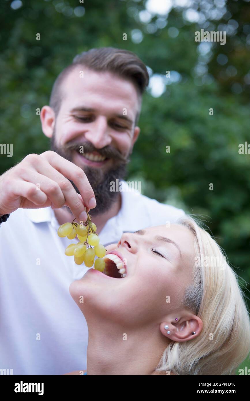 Young man feeding grapes to his wife in garden, Bavaria, Germany Stock Photo