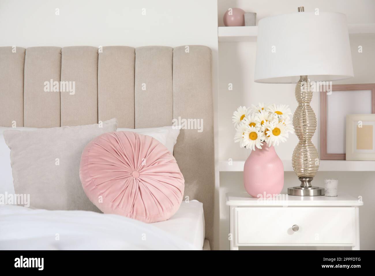 Bouquet of beautiful daisy flowers and lamp on nightstand in bedroom