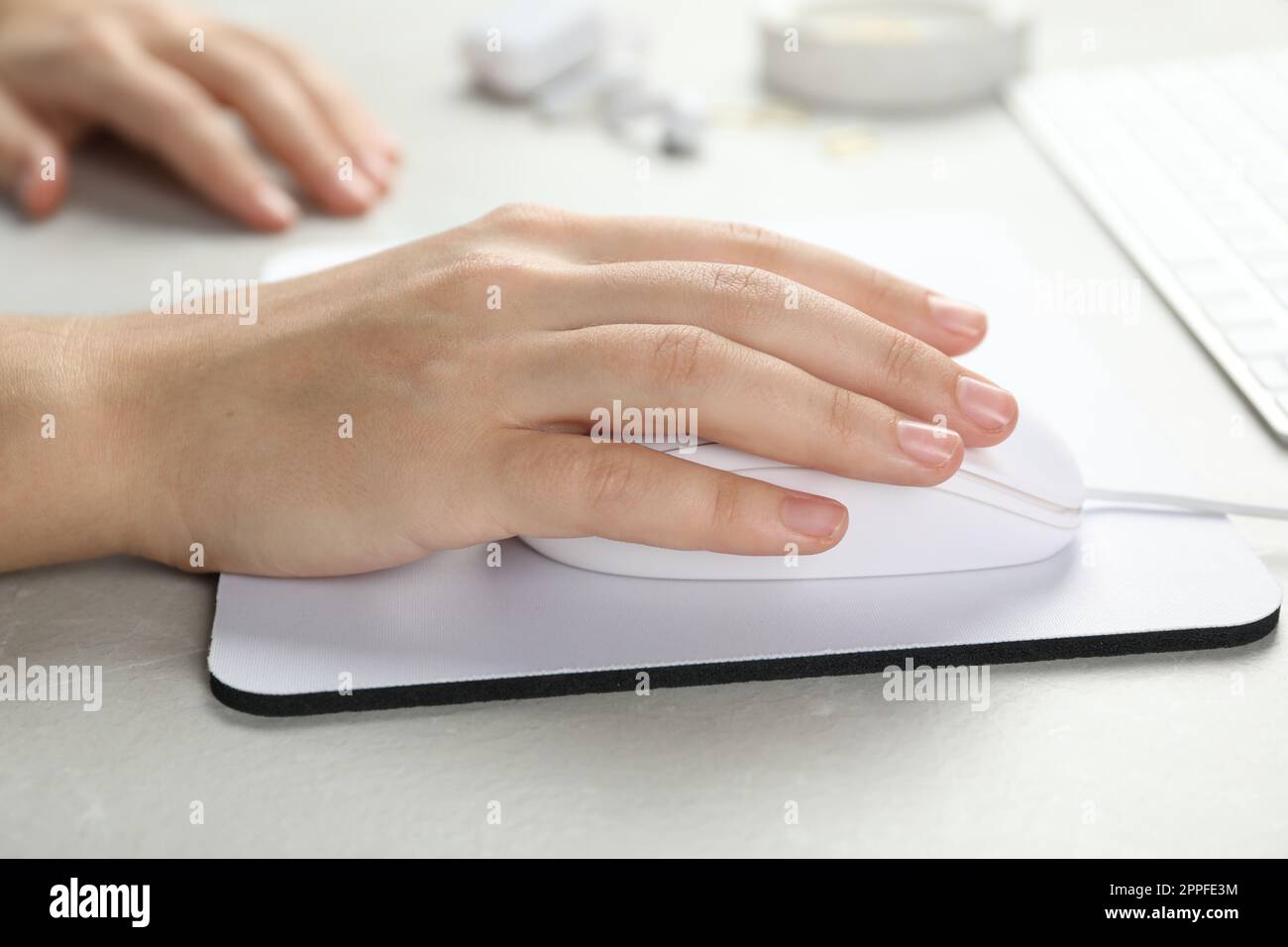 Woman using wired computer mouse on pad at light grey marble table, closeup Stock Photo