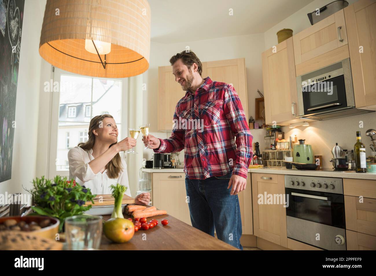 Couple celebrating with white wine in kitchen, Munich, Bavaria, Germany Stock Photo