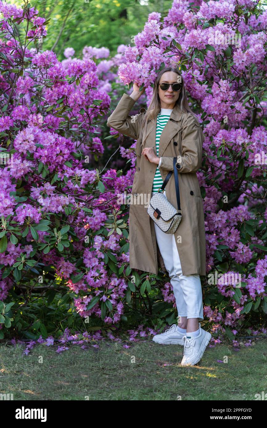 Long-haired woman in sunglasses vohle of a lushly blooming rhododendron bush Stock Photo