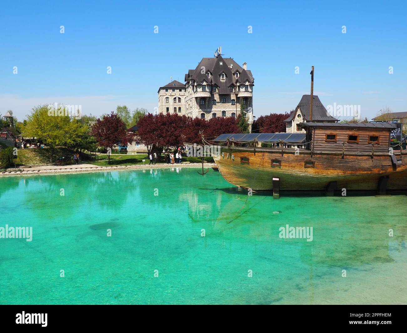 Stanisici, Bijelina, Bosnia and Herzegovina, April 25, 2021. A wooden ship with an anchor docking near the coast. Turquoise or blue water. People and tourists walk along the shore. Clear shallow water Stock Photo