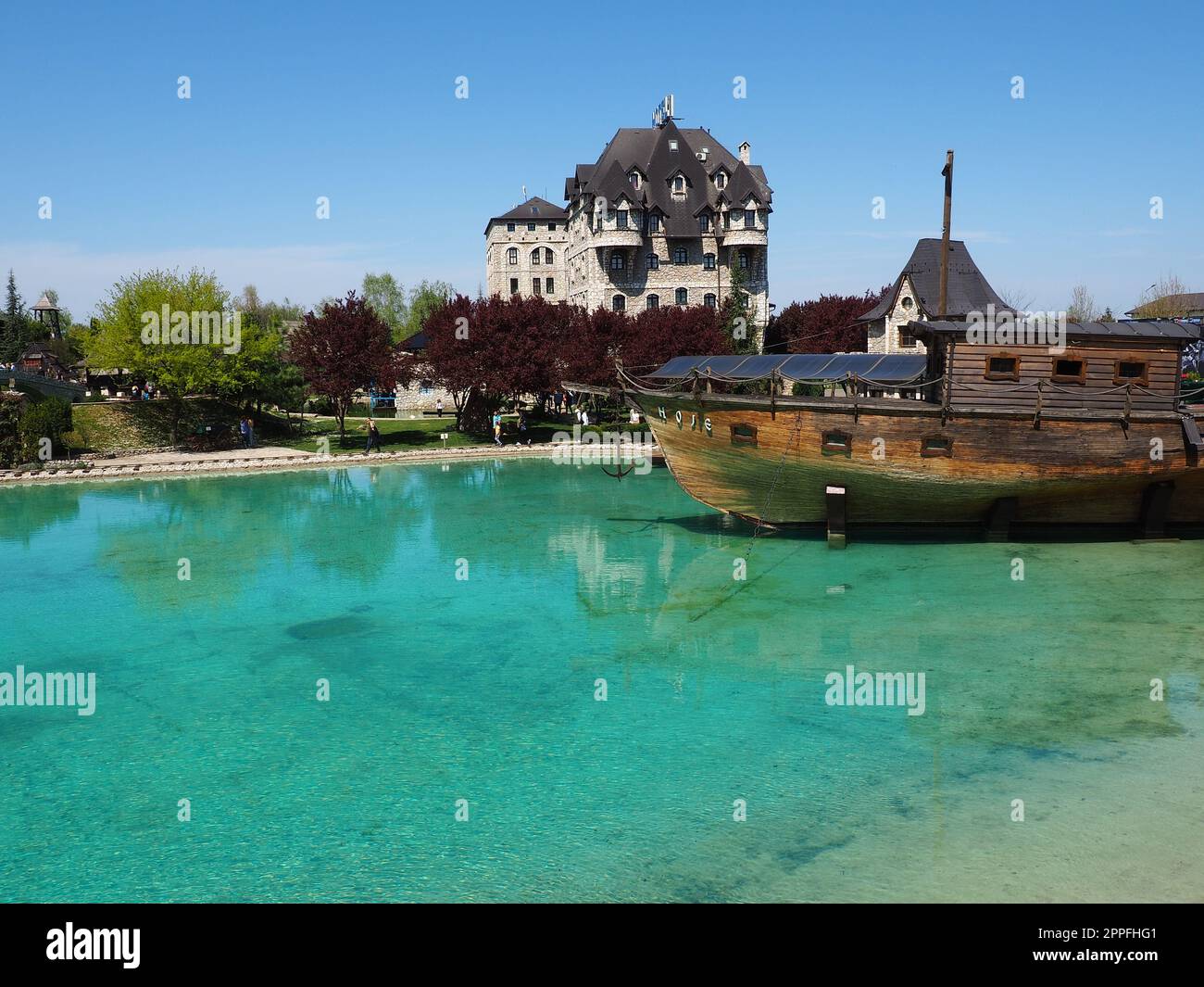 Stanisici, Bijelina, Bosnia and Herzegovina, April 25, 2021. A wooden ship with an anchor docking near the coast. Turquoise or blue water. People and tourists walk along the shore. Clear shallow water Stock Photo