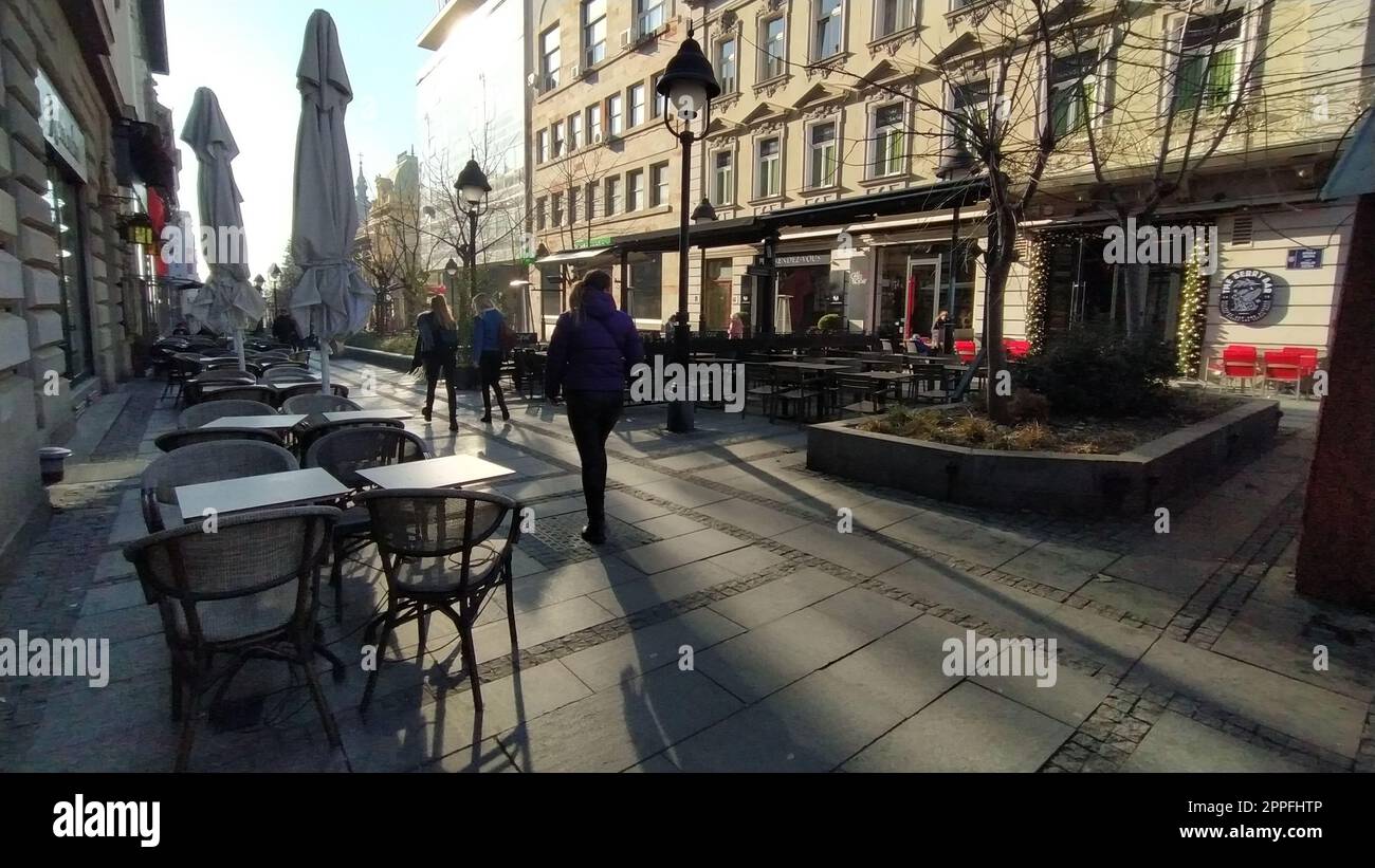 Belgrade, Serbia - January 24, 2020: morning street in the city center. People rush about their business. Street cafes are still closed. Tables, chairs and umbrellas. Girls walk energetically Stock Photo