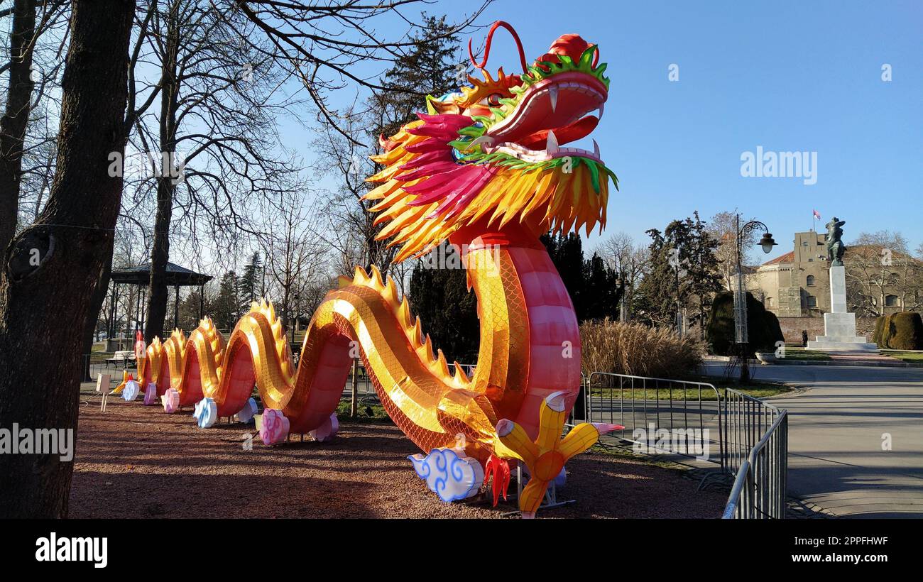 Chinese New Year. Bright red-orange dragon in the park. Traditional Chinese holiday decoration. The dragon's mouth is open. Long curly tail. Lunar-solar calendar. Spring Festival Stock Photo