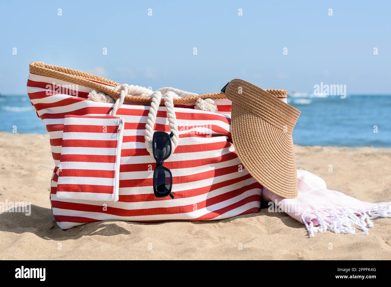 Stylish striped bag with visor cap, sunglasses and blanket on sandy beach  near sea Stock Photo