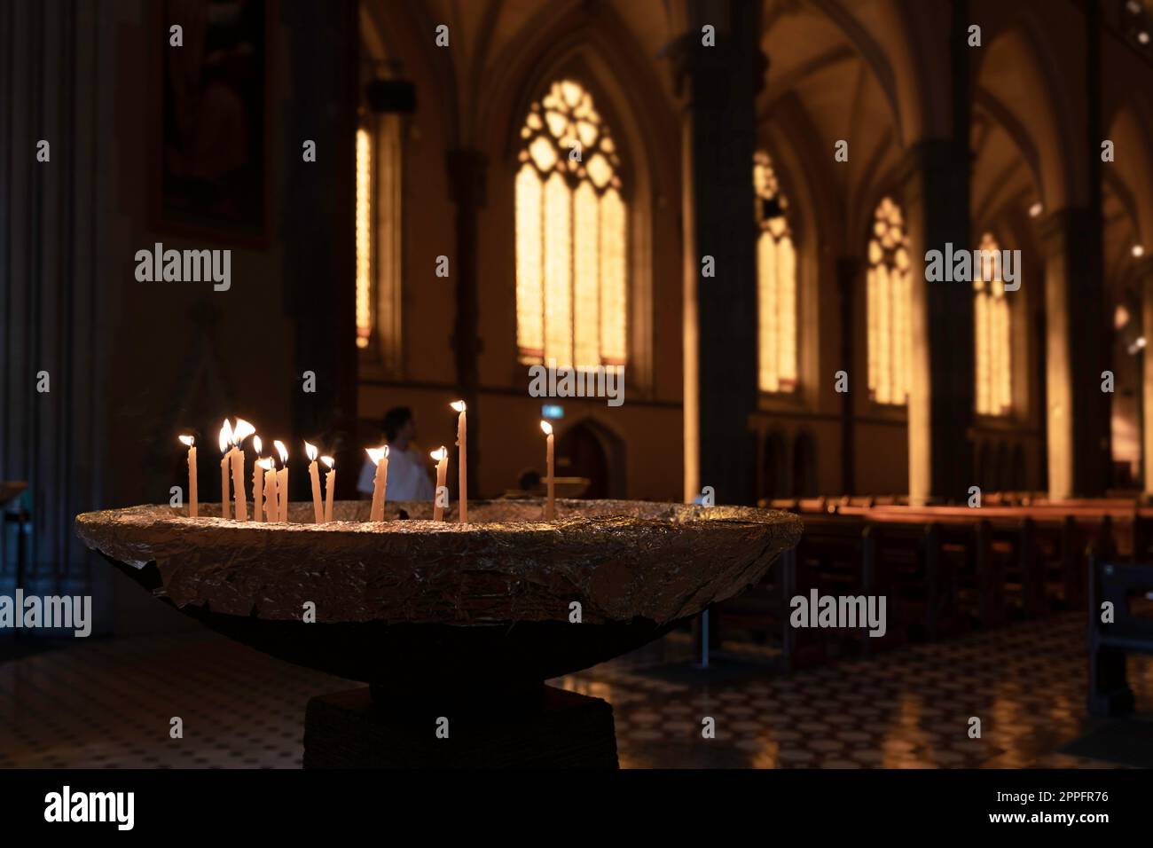 Burning candles on the edge of a baptismal font at St. Patrick's Cathedral in Melbourne, Australia. Atmospheric light enters through the church window Stock Photo