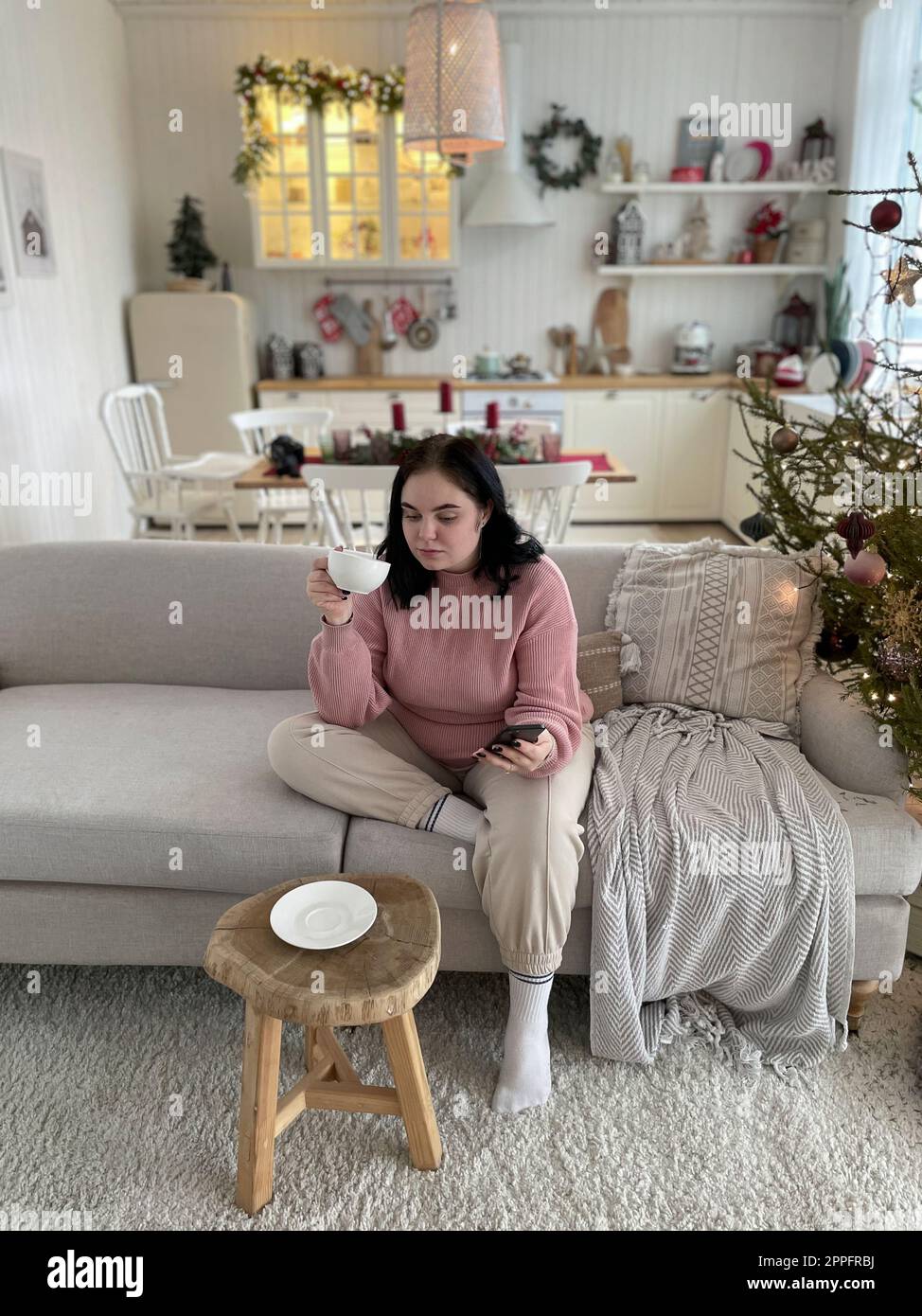 Young girl drinks coffee and holding smartphone sitting on a couch Stock Photo