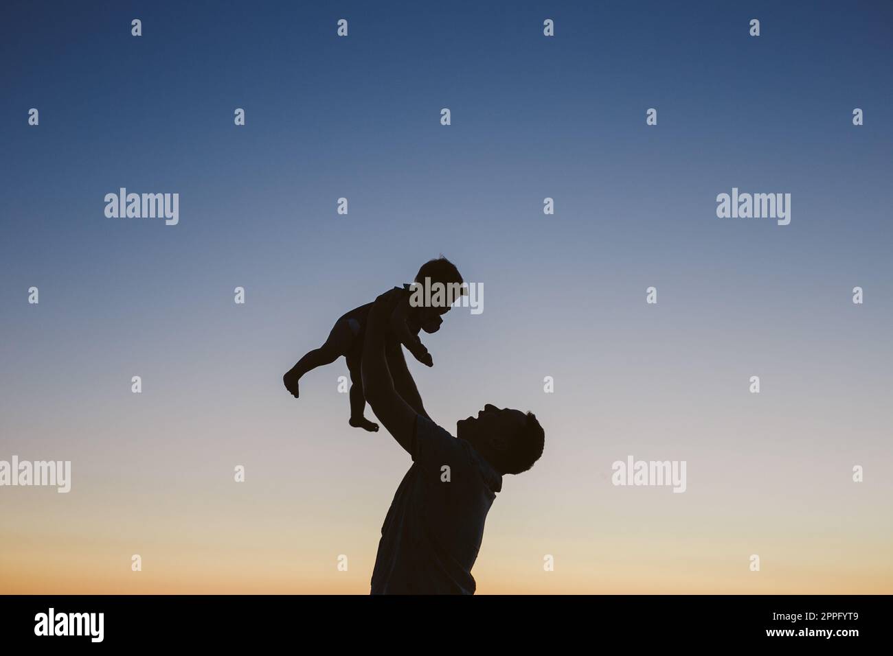 silhouette of dad holding baby in the air at sunset Stock Photo