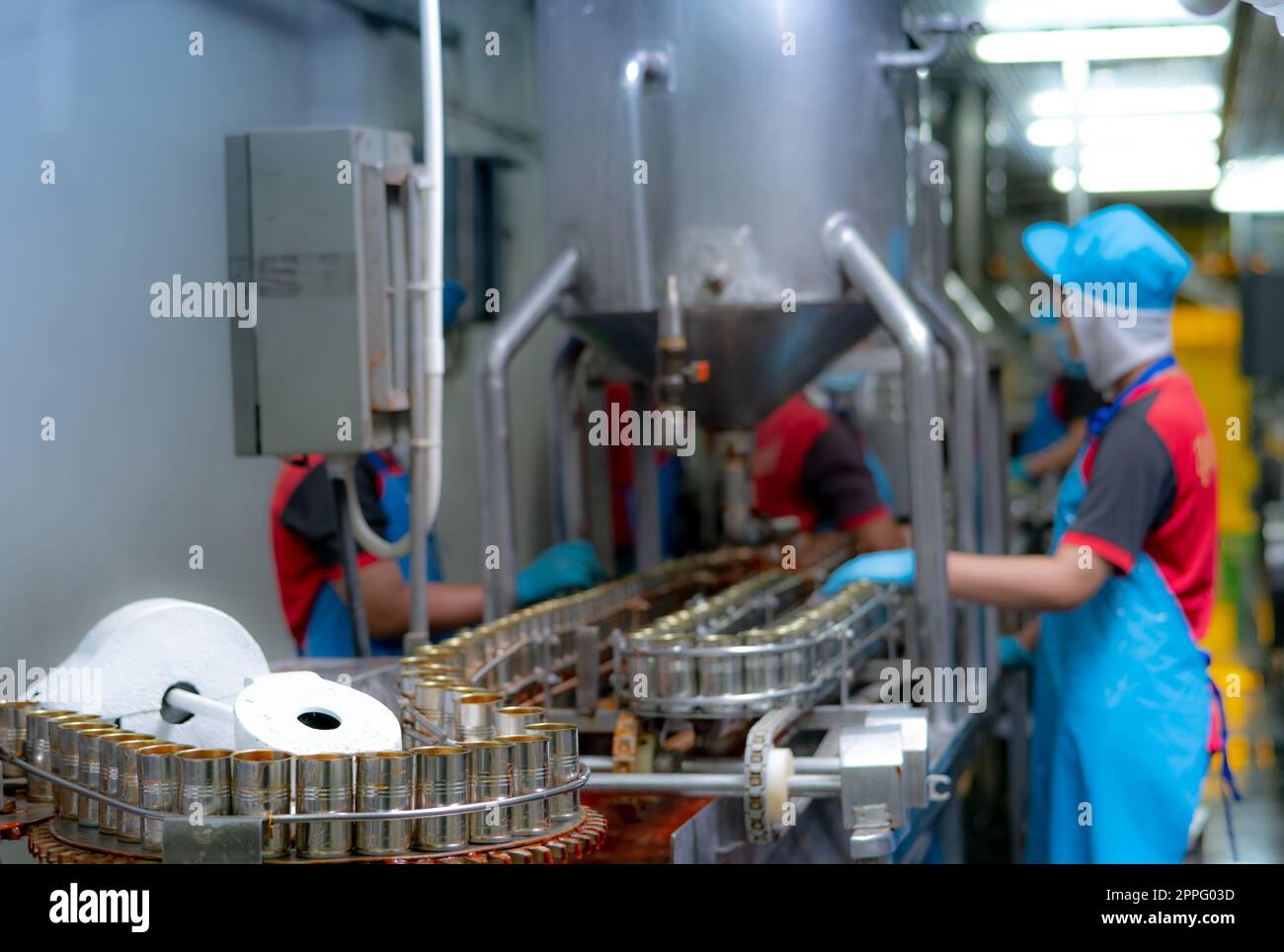 Canned fish factory. Food industry.  Sardines in red tomato sauce in tinned cans on conveyor belt at food factory. Blur workers working in food processing production line. Food manufacturing industry. Stock Photo