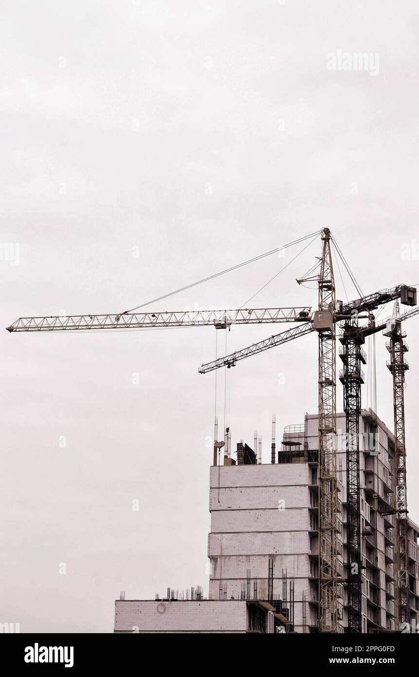 Working tall cranes inside place for with tall buildings under construction against a clear blue sky. Crane and building working progress. Retro tone Stock Photo