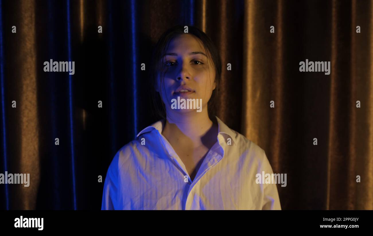 Nervous woman in white shirt in blue and yellow light breathing deeply with focus breathing, calming down after quarrel, Concept of abuse in relationships. Mental and physical violance woman Stock Photo
