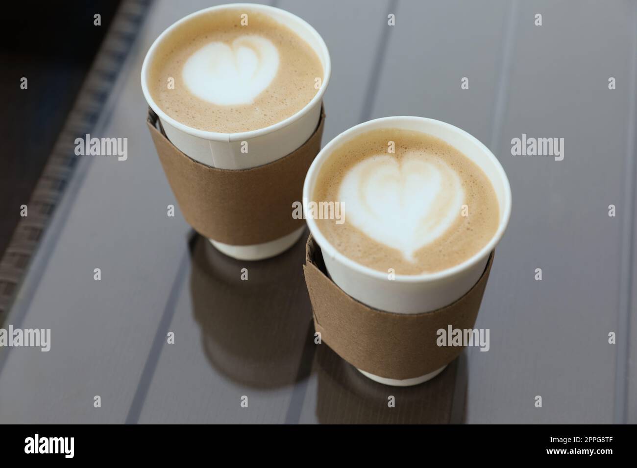 Paper takeaway cups of coffee with cardboard sleeves on glass table ...