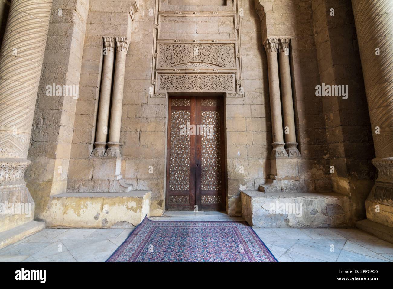 External old decorated bricks stone wall with arabesque decorated wooden door framed by stone ornate cylindrical columns Stock Photo