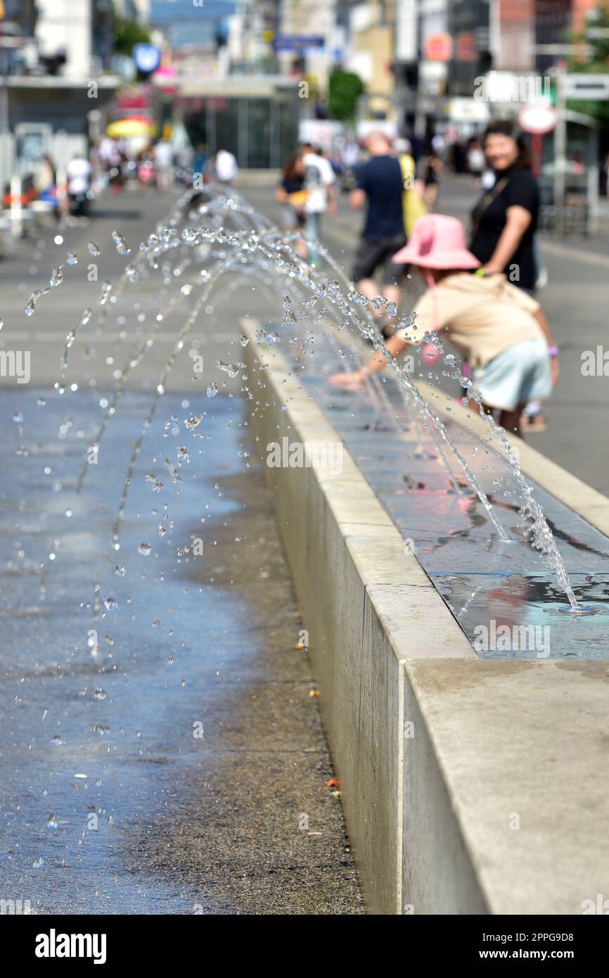 Ein MÃ¤dchen kÃ¼hlt sich an einem Wasserspiel in Wien (Bezirk Favoriten) ab - A girl cools off at a water feature in Vienna (Favoriten district) Stock Photo