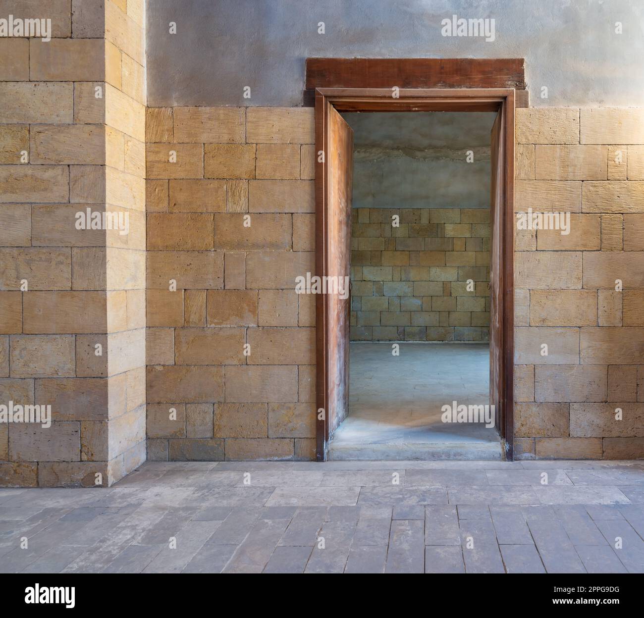Open wooden door in bricks stone wall revealing vacant room with bricks