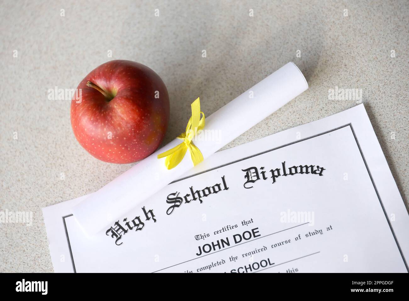 A high school diploma lies on table with small scroll and red apple. Education documents Stock Photo