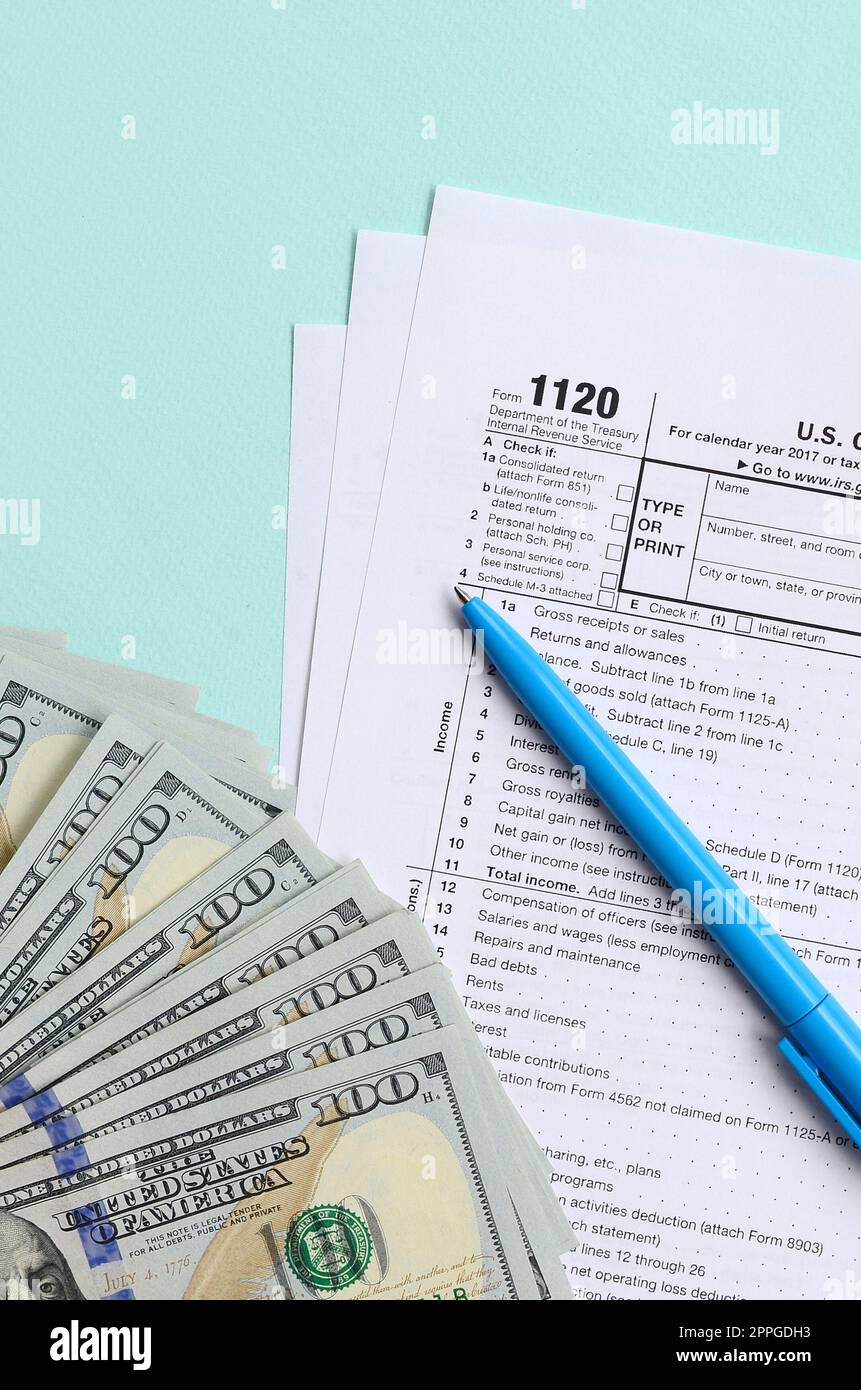 1120 tax form lies near hundred dollar bills and blue pen on a light ...