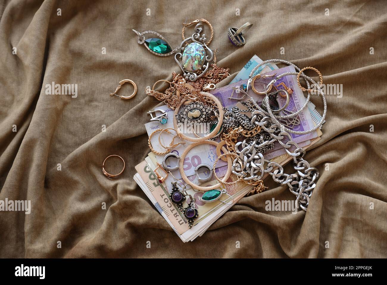 Bunch of stolen jewelry and money on military uniform cloth fabric. Looting by Russian soldiers in the Ukrainian cities during the Russian attack on Ukraine. Marauders and looters Stock Photo