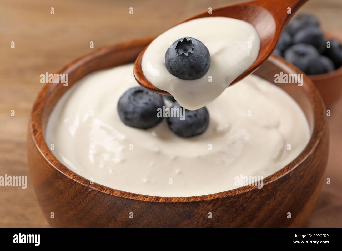 Eating tasty yogurt with blueberries from bowl on wooden table, closeup Stock Photo