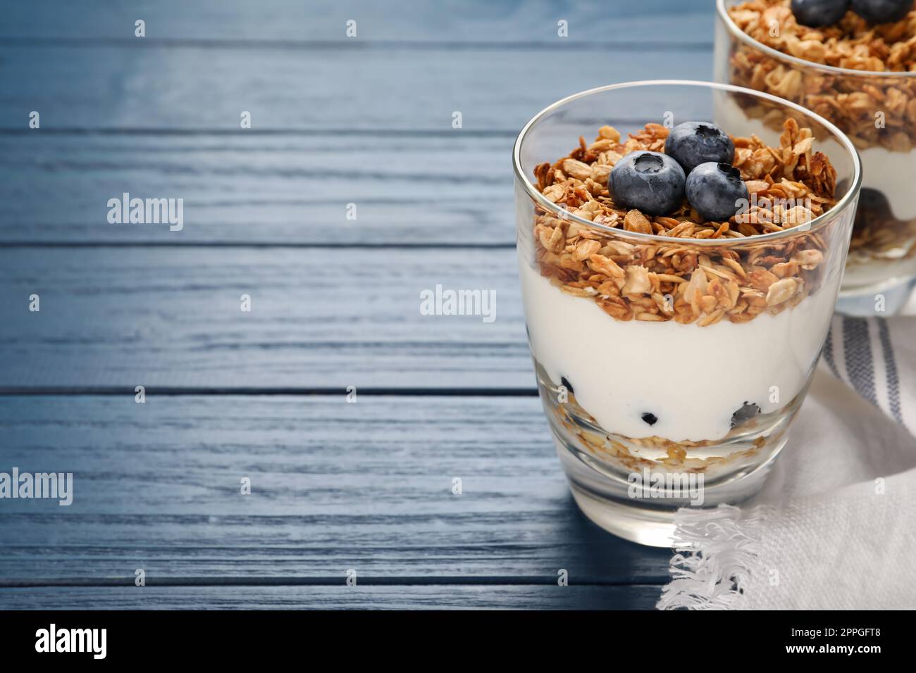 Glasses of tasty yogurt with muesli and blueberries on blue wooden table. Space for text Stock Photo