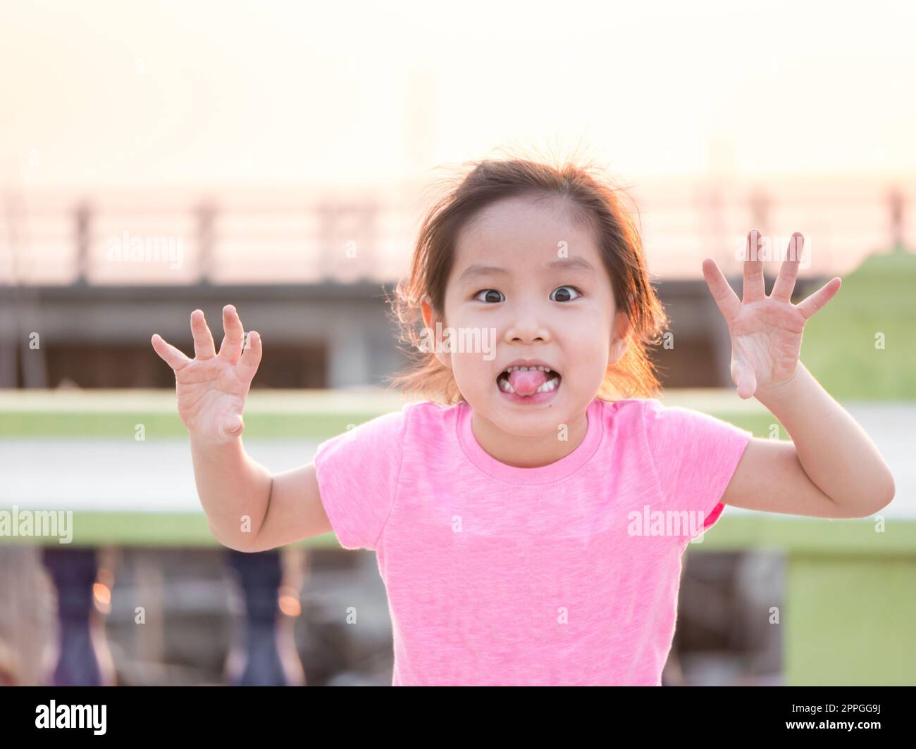 Young cute cheeky girl , holding hands up with five fingers wearing pink t shirt,sticking out her tongue for funny face Stock Photo