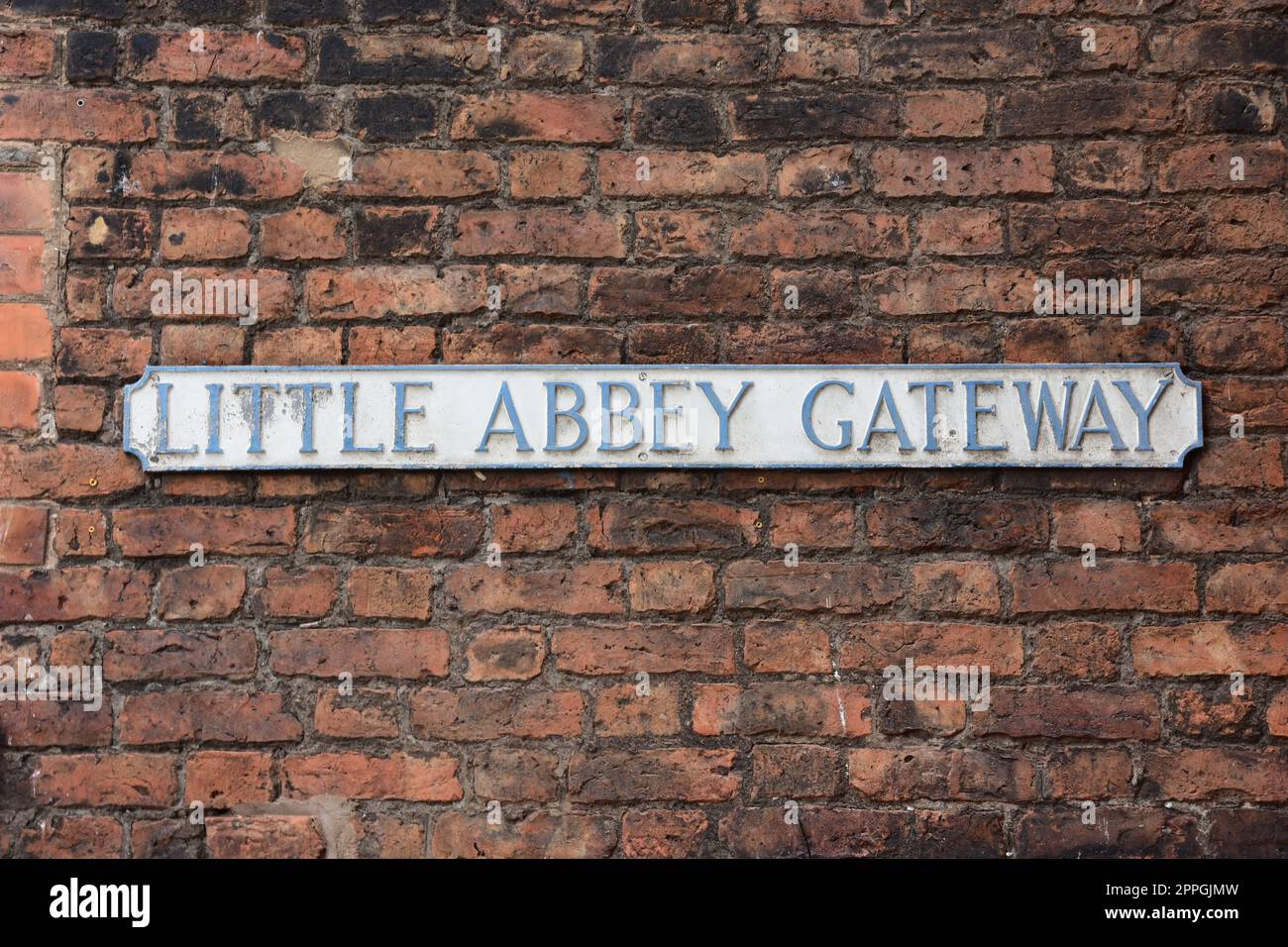 Faded street name sign for Little Abbey Gateway mounted on a red brick wall Stock Photo