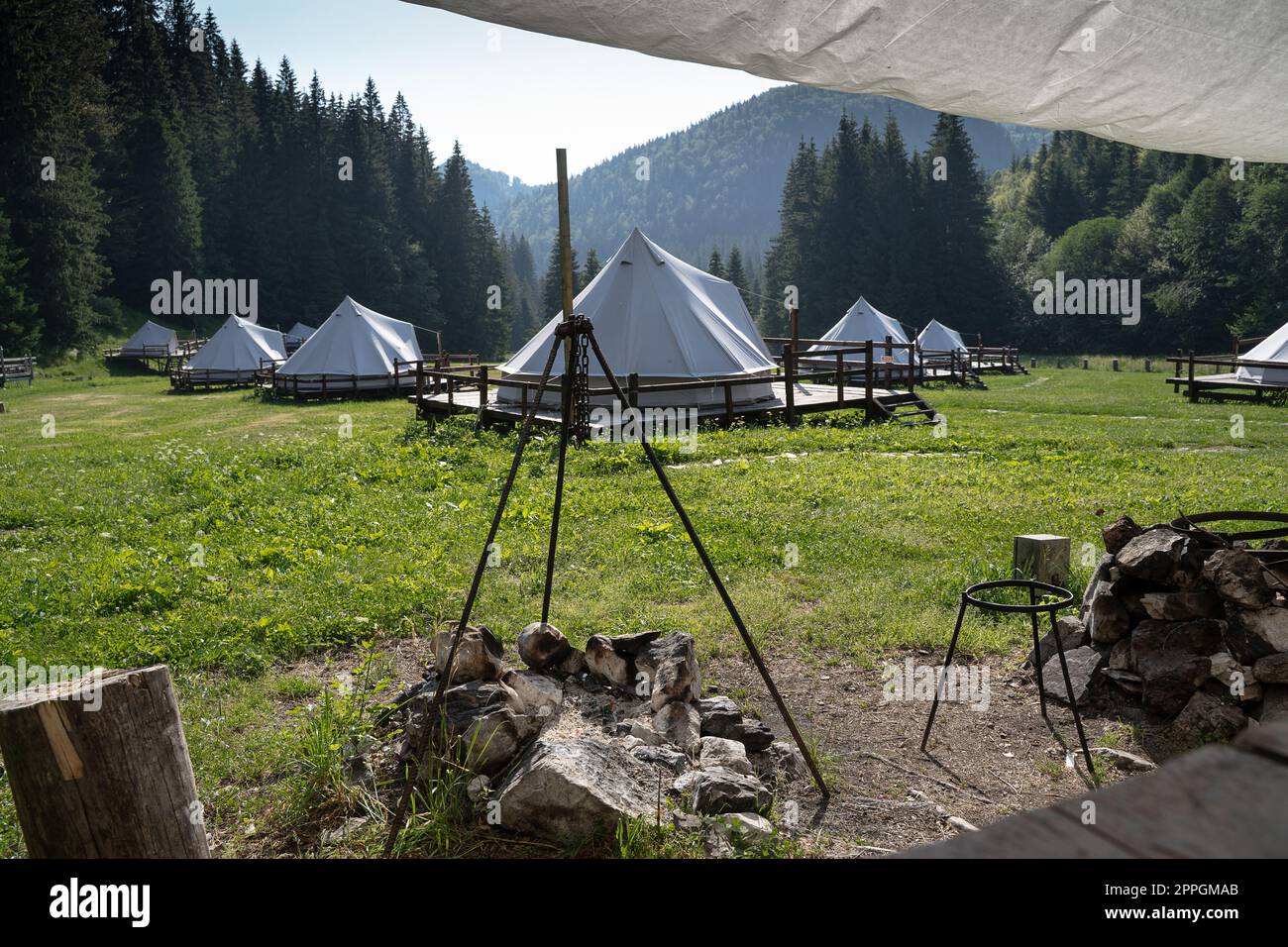 cooking area with fireplace in glamping tent camp site in green meadow surrounded by fir tree forest Stock Photo