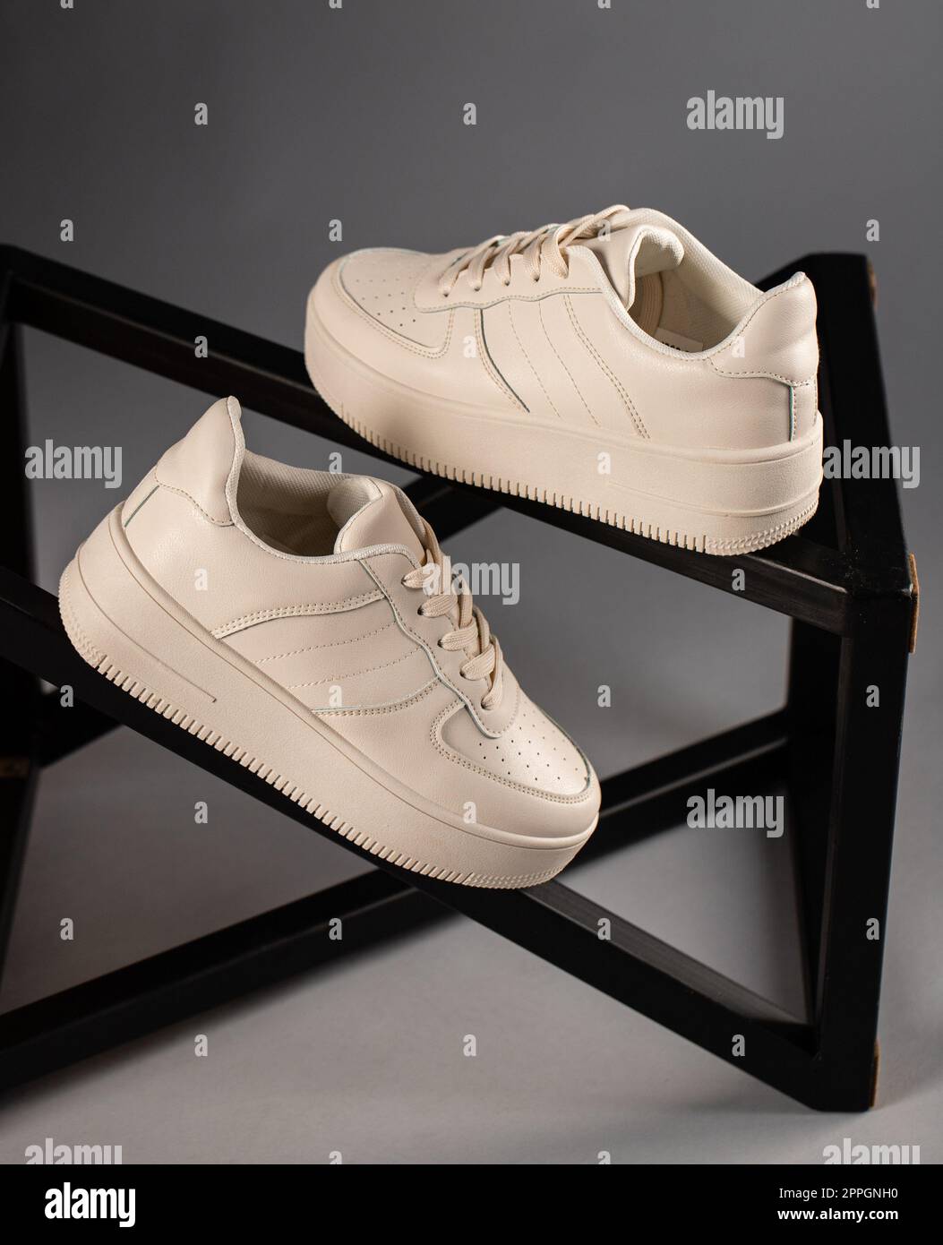 Pair of stylish white women's sneakers standing on metal structure on gray background. Stock Photo