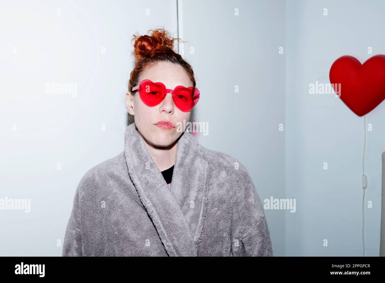 Woman with heart-shaped glasses and bathrobe in room Stock Photo