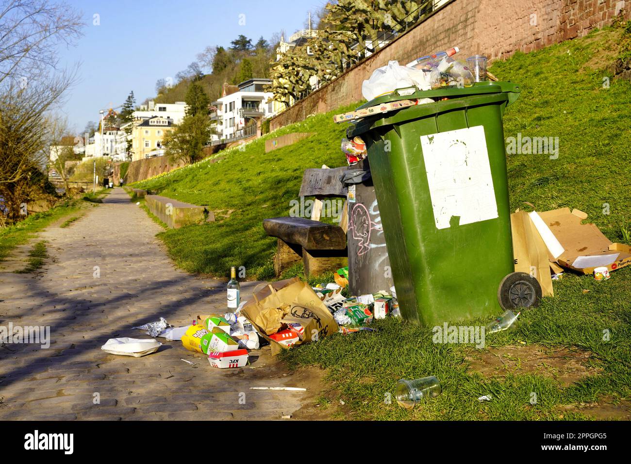 Littering in a park beside a bench and a full dustbin. Heidelberg