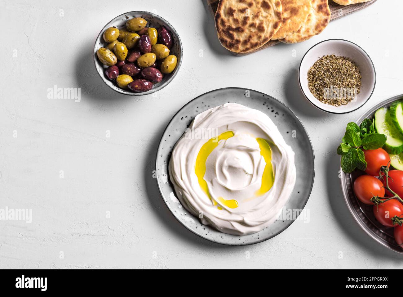 Labneh yogurt cream cheese with olive oil, zaatar, olives, vegetables and pita bread on white