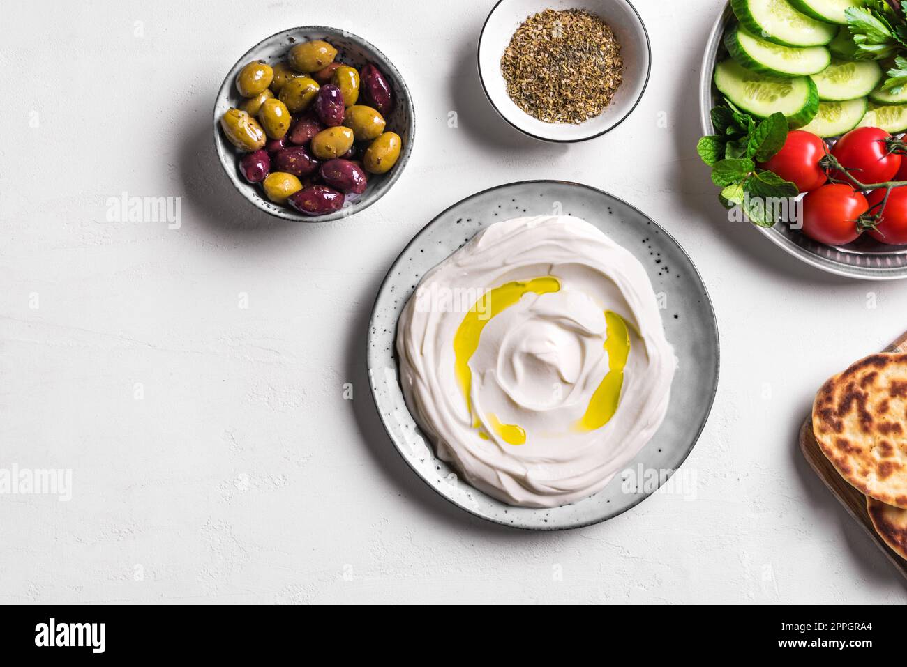 Labneh yogurt cream cheese with olive oil, zaatar, olives, vegetables and pita bread on white