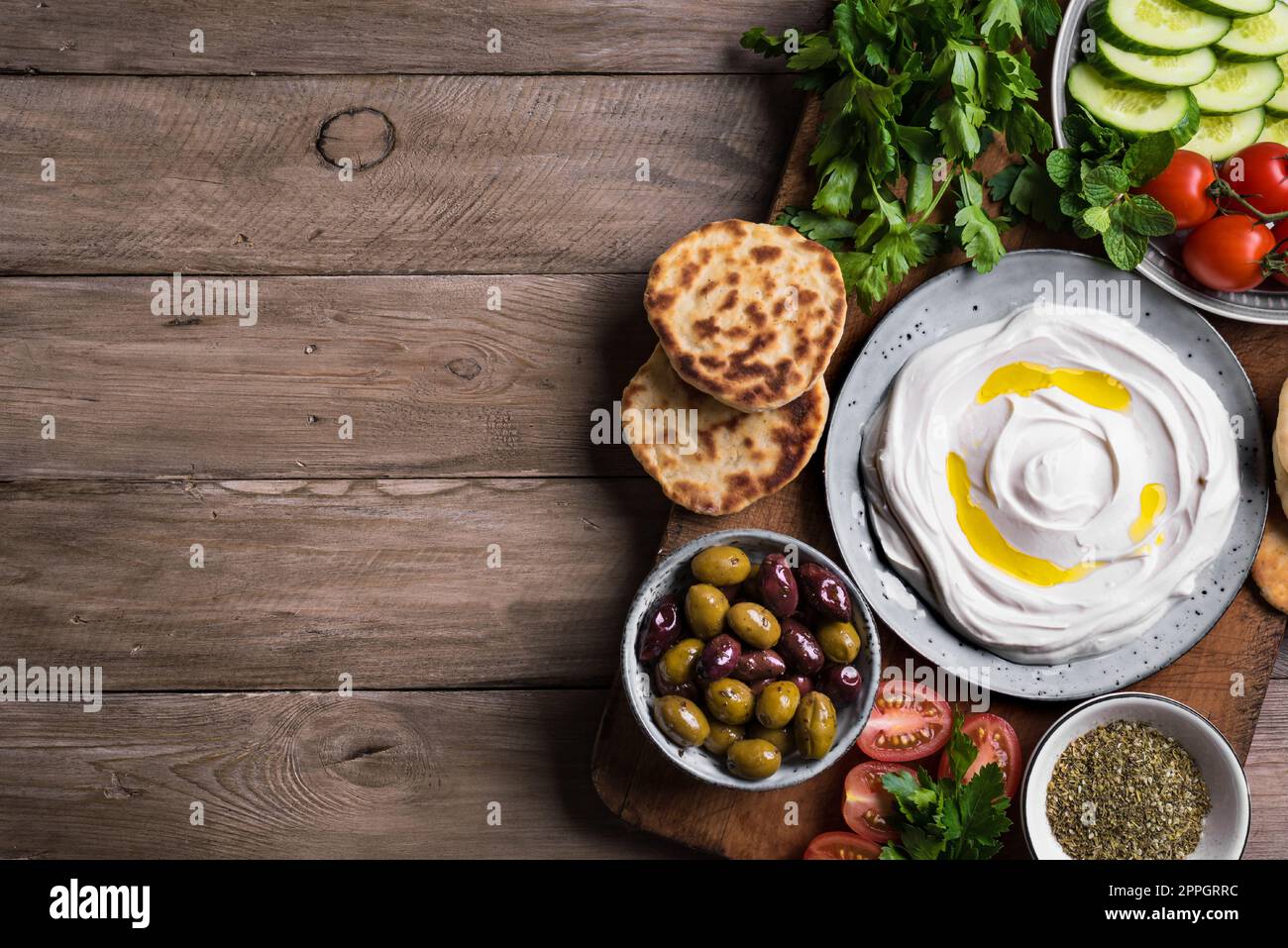 Labneh yogurt cream cheese with olive oil, zaatar, olives, vegetables and pita bread on white