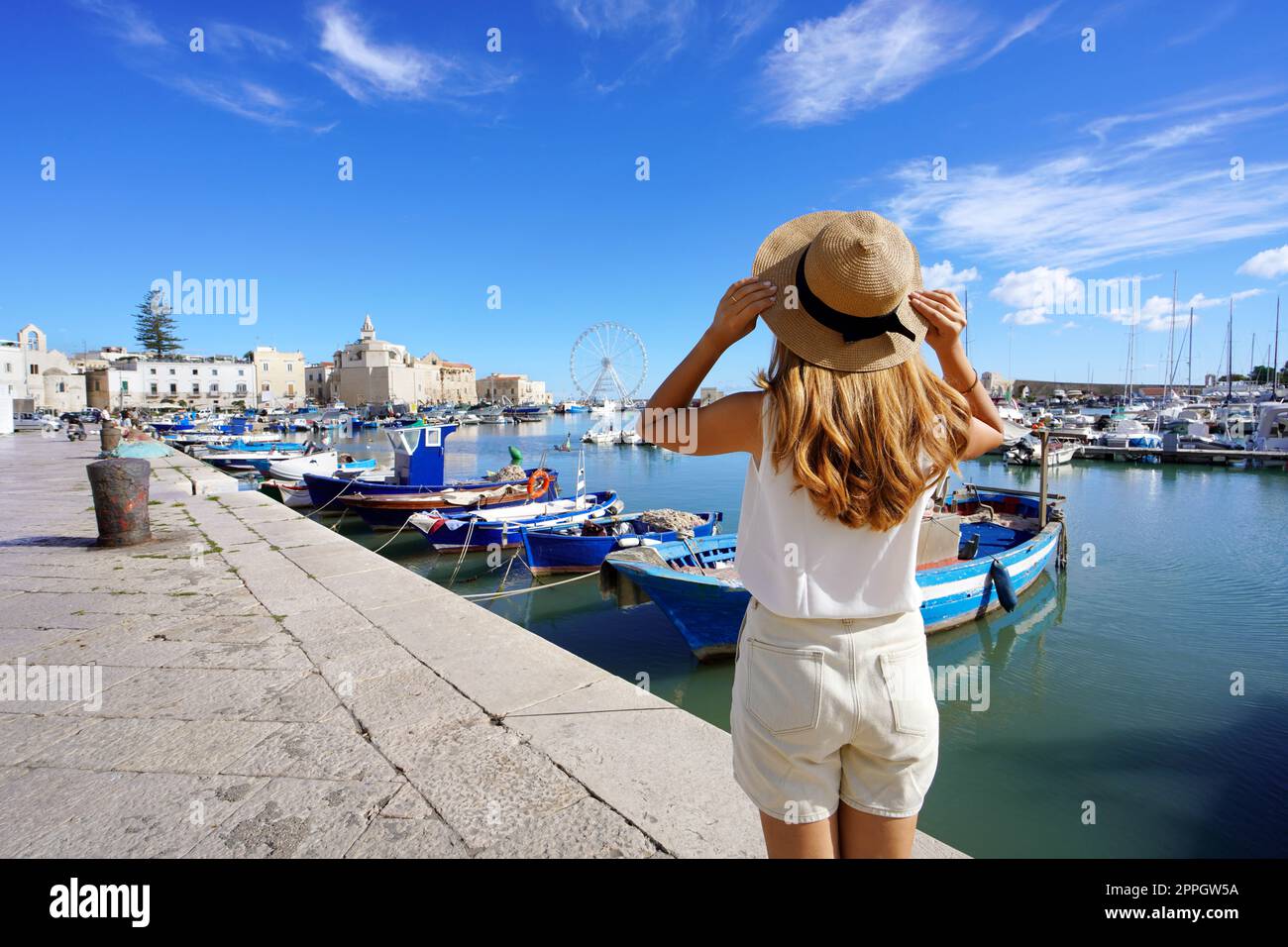 Holidays in Apulia. Back view of beautiful traveler girl enjoying view of Trani historic town and seaport. Summer vacation in Italy. Stock Photo