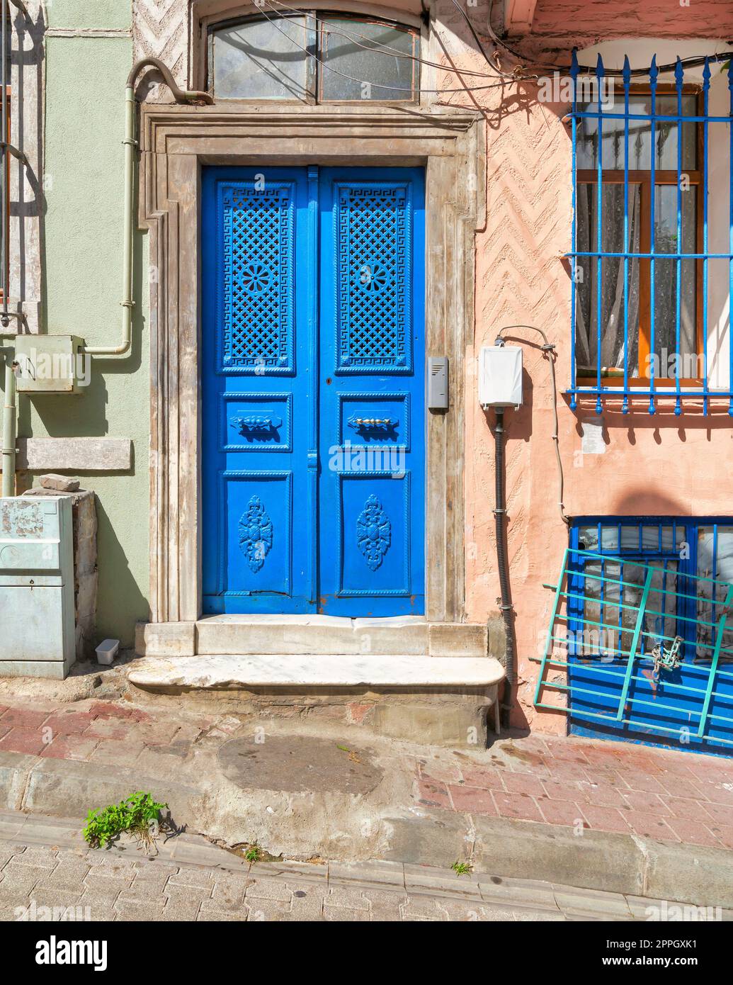 Blue painted decorated metal door and wrought iron window in a stone wall painted in orange and green on city street Stock Photo