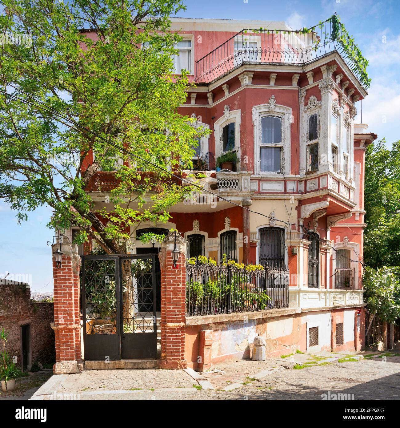 Old red house, with wrought iron windows, balconies and green trees, Balat district, Istanbul, Turkey Stock Photo